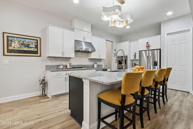 kitchen with white cabinets, light wood-type flooring, stainless steel appliances, and an island with sink