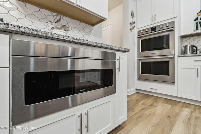 kitchen featuring light wood-type flooring, backsplash, light stone counters, double oven, and white cabinets