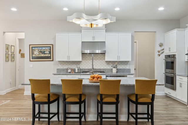 kitchen featuring an island with sink, light hardwood / wood-style floors, white cabinetry, stainless steel appliances, and extractor fan