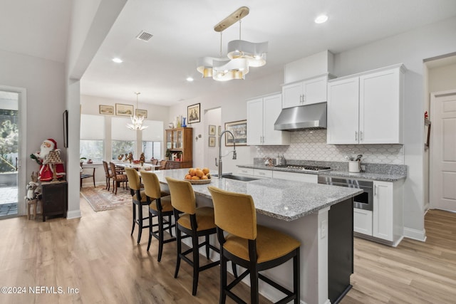 kitchen with white cabinets, light wood-type flooring, sink, and an island with sink