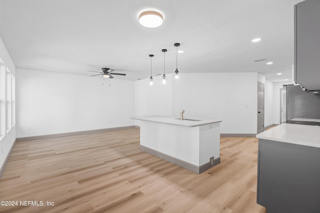 kitchen with refrigerator, a sink, baseboards, light countertops, and light wood-type flooring