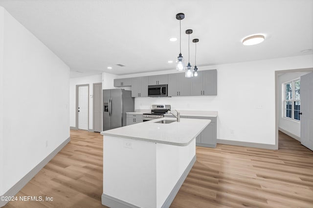 kitchen featuring stainless steel appliances, a sink, light wood-style floors, light countertops, and decorative light fixtures