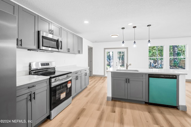 kitchen with gray cabinetry, stainless steel appliances, a sink, light wood-style floors, and light countertops