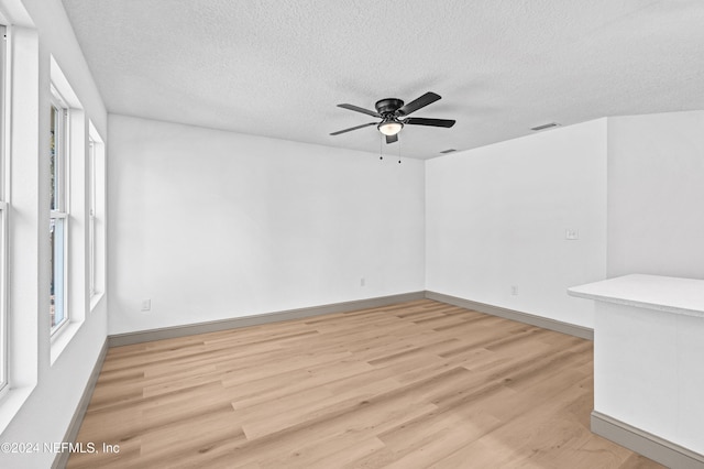 spare room with baseboards, light wood-style flooring, visible vents, and a textured ceiling