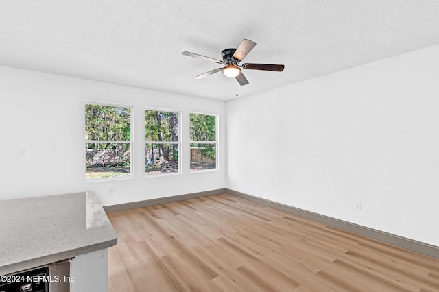 empty room with light wood-style floors, ceiling fan, a textured ceiling, and baseboards