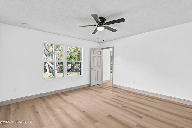 spare room featuring light wood-style floors, ceiling fan, a textured ceiling, and baseboards