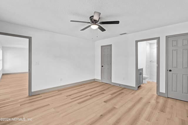 unfurnished bedroom with light wood-style flooring, connected bathroom, visible vents, and a textured ceiling