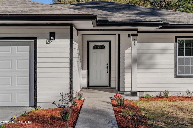 entrance to property with a garage and a shingled roof