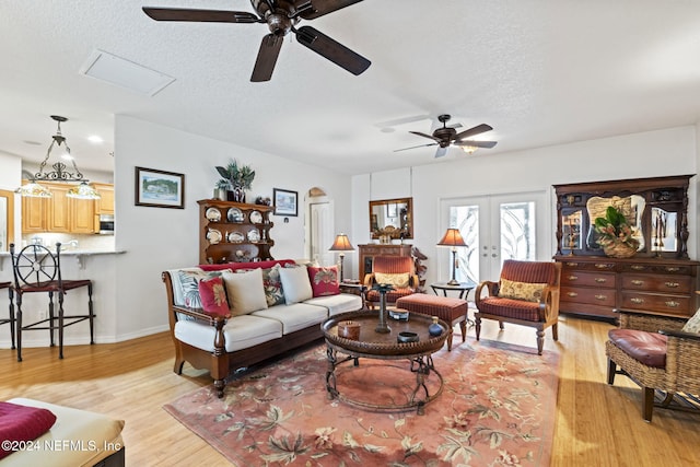 living room with a textured ceiling, ceiling fan, light hardwood / wood-style flooring, and french doors