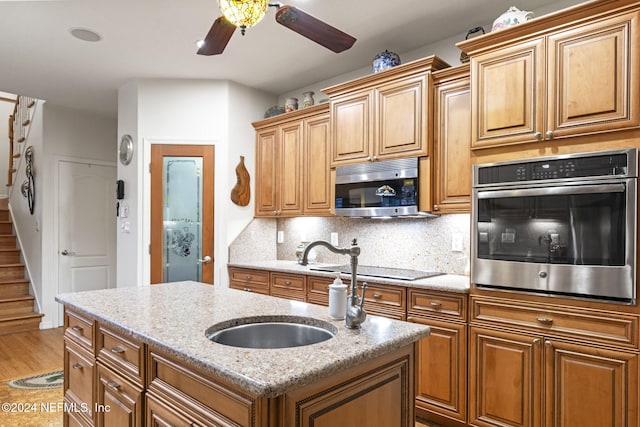 kitchen featuring light stone countertops, appliances with stainless steel finishes, tasteful backsplash, a kitchen island with sink, and sink