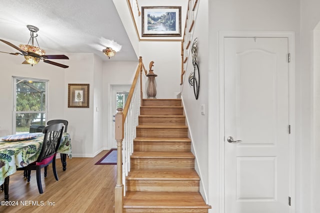 stairs with hardwood / wood-style floors, a textured ceiling, ceiling fan, and a healthy amount of sunlight