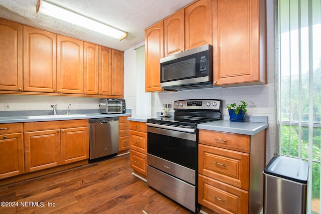 kitchen with sink, dark hardwood / wood-style floors, backsplash, a textured ceiling, and appliances with stainless steel finishes