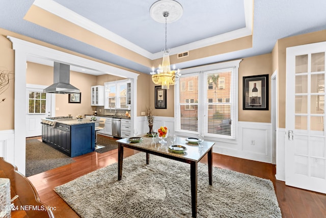 dining space with ornamental molding, a raised ceiling, dark wood-type flooring, sink, and an inviting chandelier