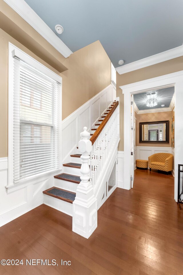 stairs with wood-type flooring, ornamental molding, and an inviting chandelier