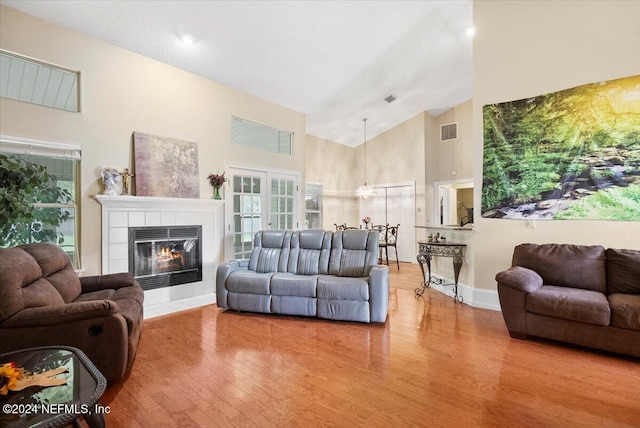 living room featuring a tile fireplace, hardwood / wood-style floors, high vaulted ceiling, and french doors