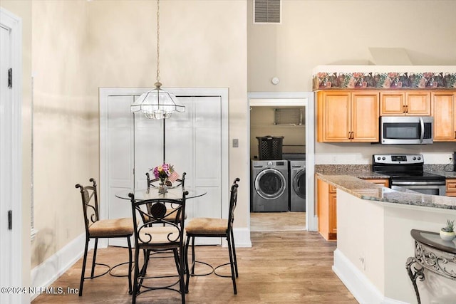 kitchen featuring hanging light fixtures, an inviting chandelier, light hardwood / wood-style floors, washer and dryer, and appliances with stainless steel finishes