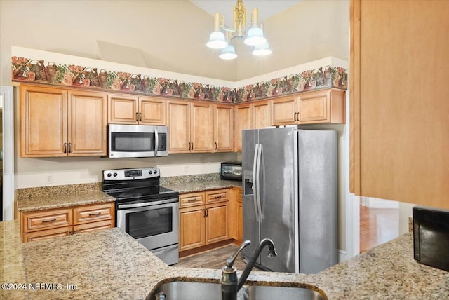 kitchen featuring light stone countertops, appliances with stainless steel finishes, sink, pendant lighting, and a notable chandelier