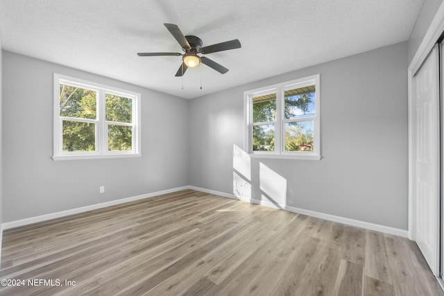 unfurnished bedroom with multiple windows, a textured ceiling, light wood-type flooring, and ceiling fan