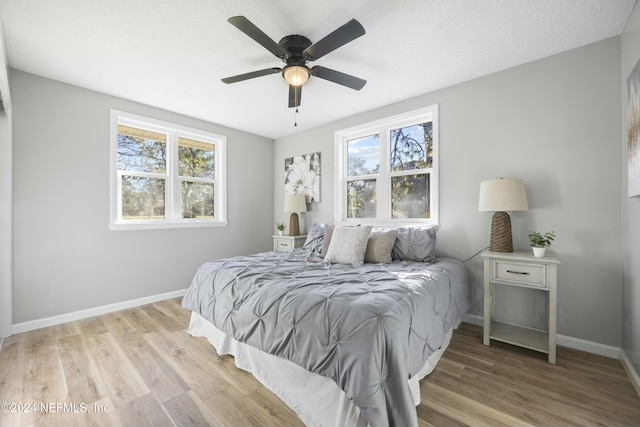 bedroom with ceiling fan, light hardwood / wood-style floors, a textured ceiling, and multiple windows