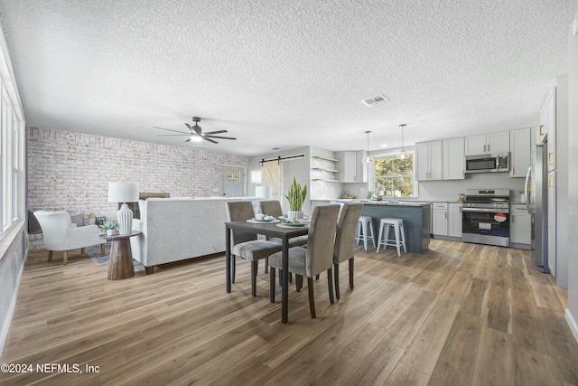 dining room with hardwood / wood-style floors, ceiling fan, a barn door, a textured ceiling, and brick wall