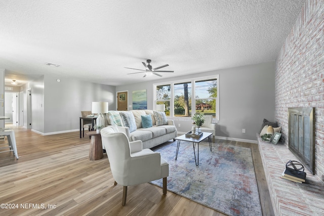 living room featuring a fireplace, a textured ceiling, light wood-type flooring, and ceiling fan