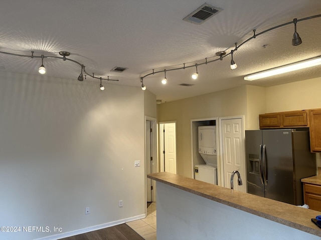 kitchen with sink, rail lighting, stainless steel fridge with ice dispenser, stacked washer / dryer, and light tile patterned floors