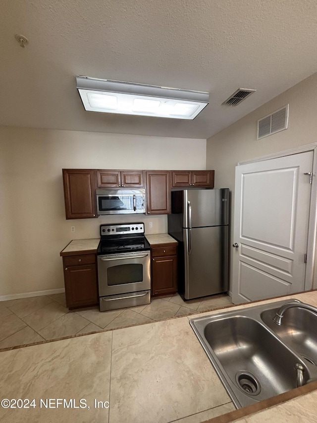 kitchen featuring a textured ceiling, stainless steel appliances, sink, lofted ceiling, and light tile patterned flooring