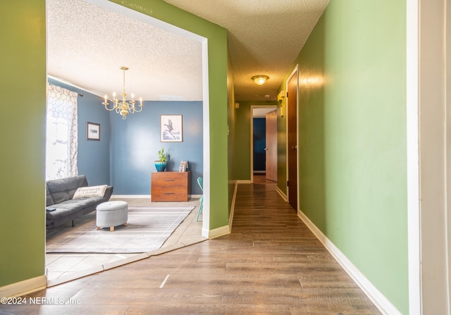 hall with wood-type flooring, a textured ceiling, and a notable chandelier