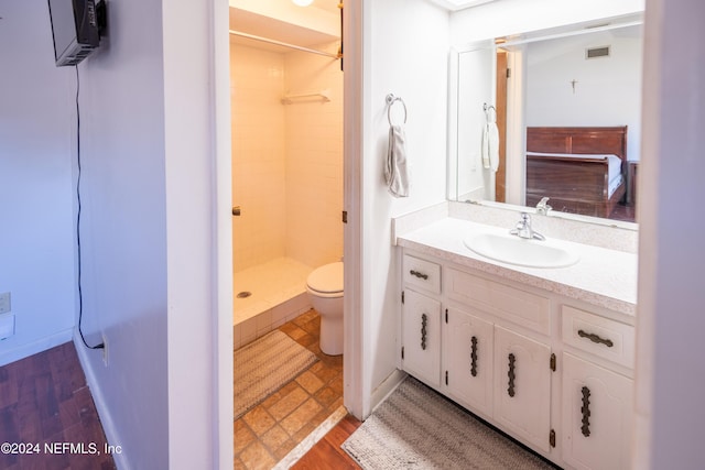 bathroom featuring a tile shower, toilet, vanity, and hardwood / wood-style flooring