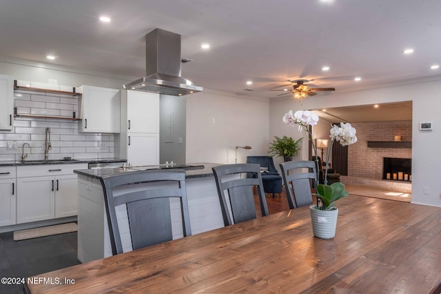 kitchen featuring sink, white cabinetry, a center island, island range hood, and a fireplace