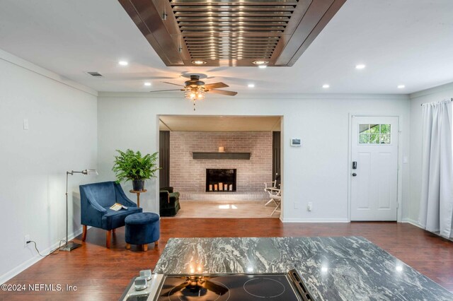 living room featuring a brick fireplace, dark wood-type flooring, ornamental molding, and ceiling fan