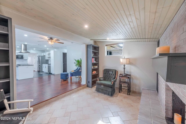 sitting room featuring a fireplace, wooden ceiling, and ceiling fan