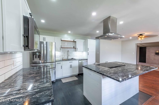 kitchen with appliances with stainless steel finishes, island range hood, white cabinetry, sink, and dark stone countertops