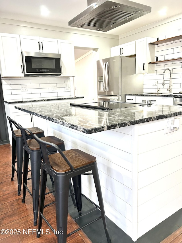 kitchen featuring white cabinetry, a breakfast bar area, stainless steel appliances, dark wood-type flooring, and wall chimney exhaust hood