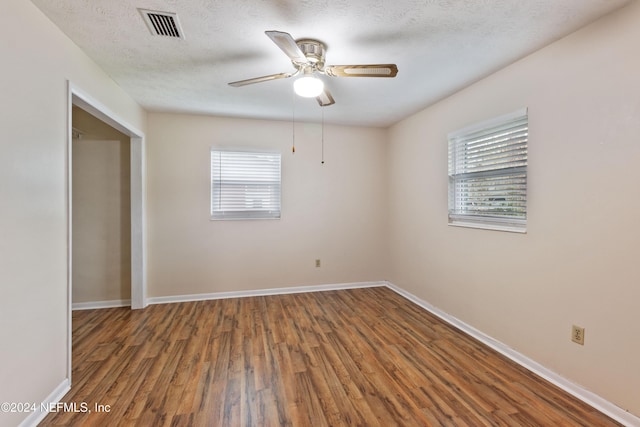 empty room with a textured ceiling, plenty of natural light, and dark hardwood / wood-style floors