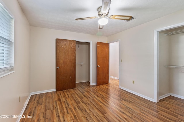 unfurnished bedroom with hardwood / wood-style floors, ceiling fan, a textured ceiling, and two closets