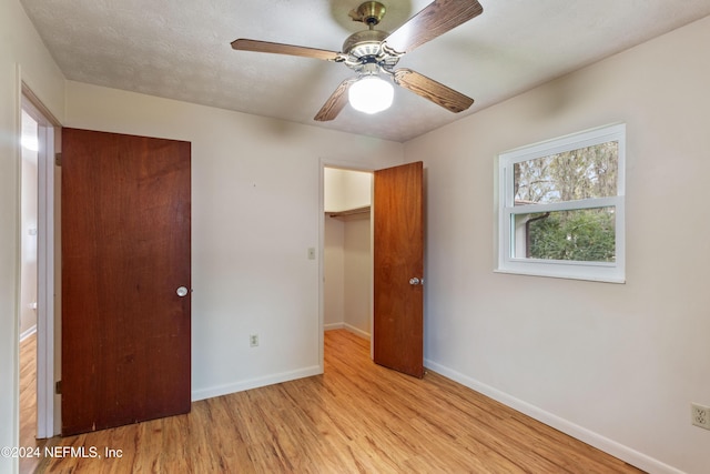 unfurnished bedroom featuring ceiling fan, a spacious closet, a textured ceiling, a closet, and light wood-type flooring