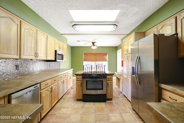 kitchen featuring a ceiling fan, light brown cabinetry, tasteful backsplash, appliances with stainless steel finishes, and a skylight