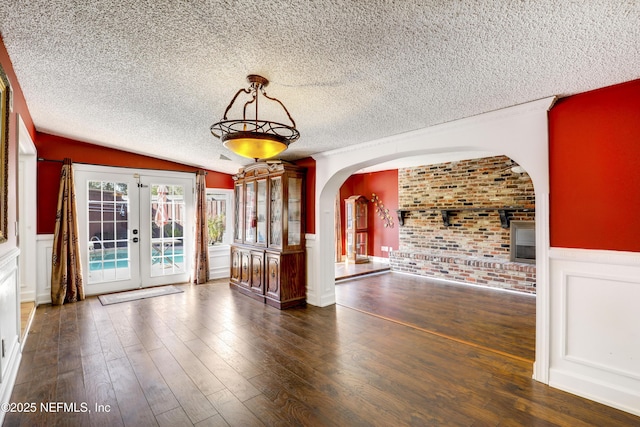 empty room featuring hardwood / wood-style floors, arched walkways, wainscoting, french doors, and a textured ceiling