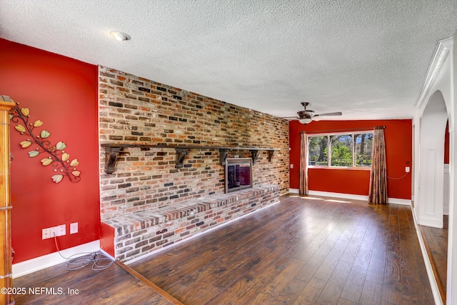 unfurnished living room with hardwood / wood-style flooring, a brick fireplace, arched walkways, and ceiling fan