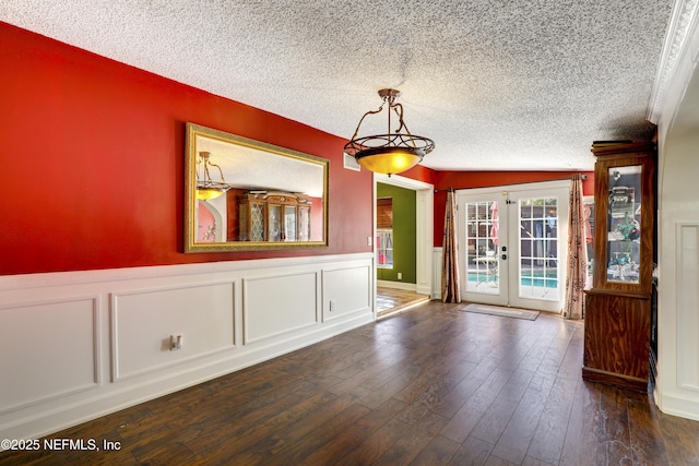 unfurnished dining area featuring french doors, a wainscoted wall, a textured ceiling, and dark wood-style floors