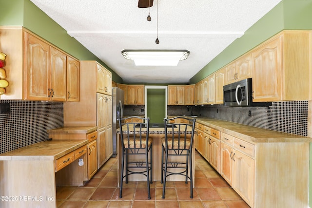 kitchen with backsplash, light brown cabinets, a breakfast bar, light tile patterned floors, and stainless steel appliances