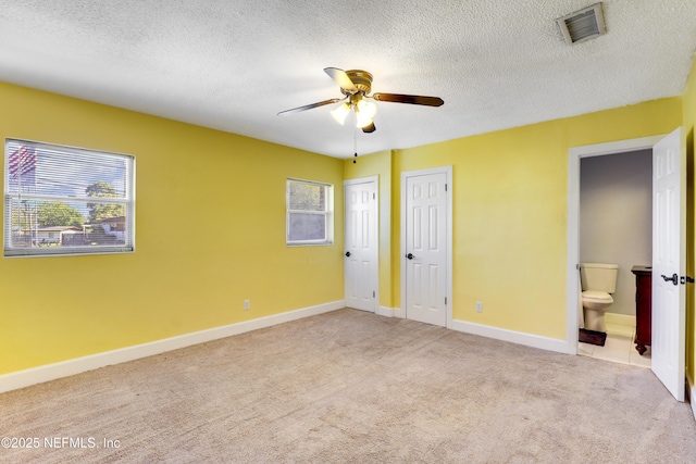 unfurnished bedroom with visible vents, two closets, carpet, a textured ceiling, and ensuite bath