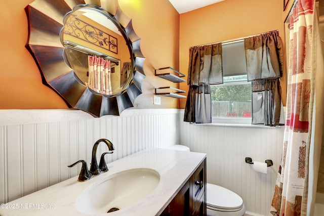 bathroom with a wainscoted wall, toilet, vanity, and a shower with curtain