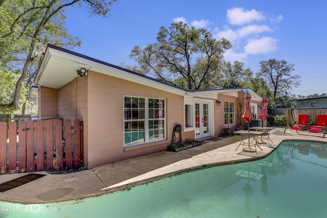 back of property with a patio, fence, french doors, a fenced in pool, and concrete block siding