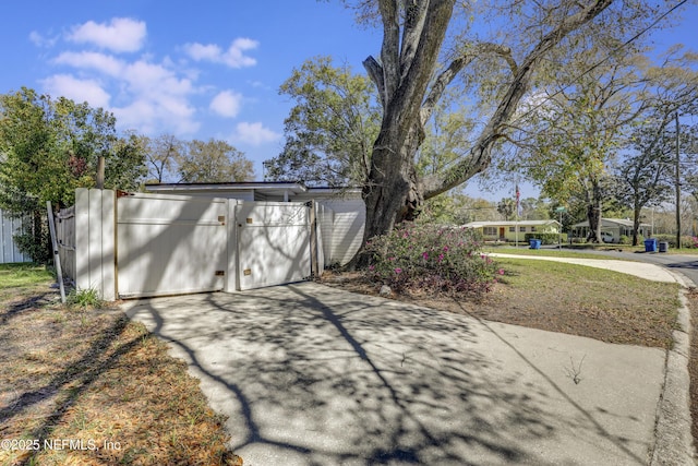 exterior space with concrete driveway, a gate, fence, and a garage