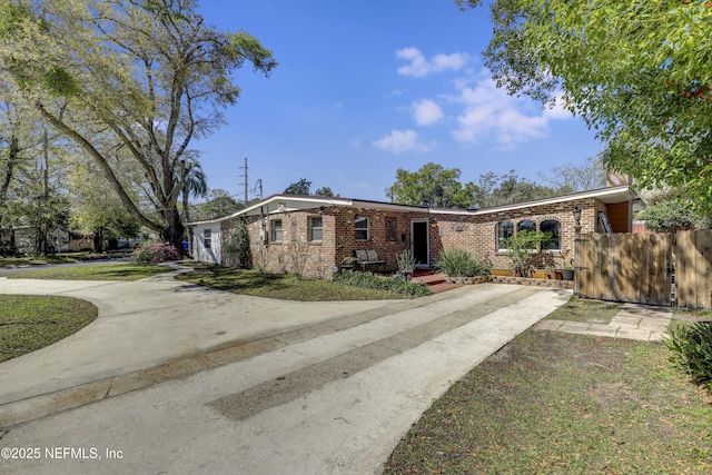 view of front of property featuring brick siding, driveway, and fence