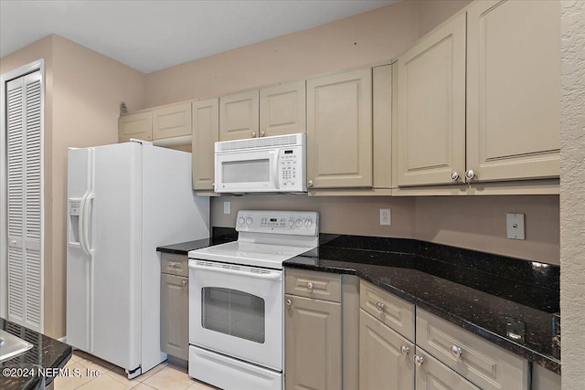 kitchen with light tile patterned floors, white appliances, and dark stone counters