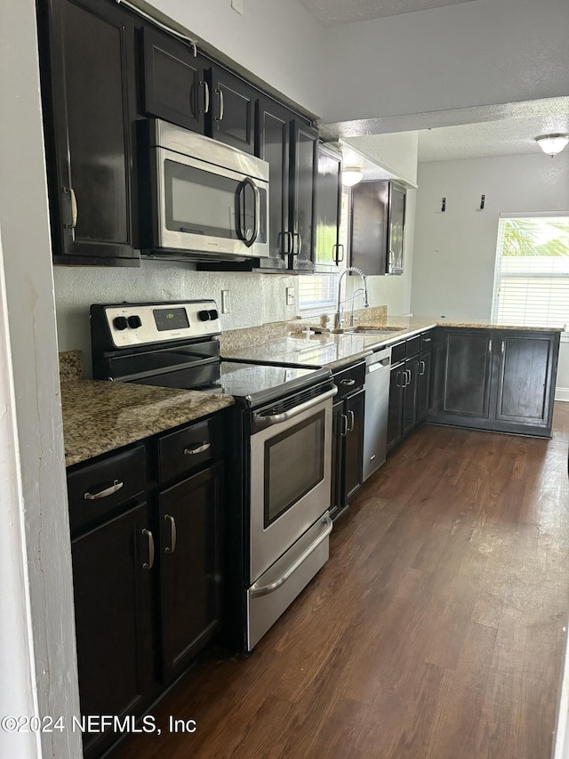 kitchen with kitchen peninsula, appliances with stainless steel finishes, dark wood-type flooring, and sink