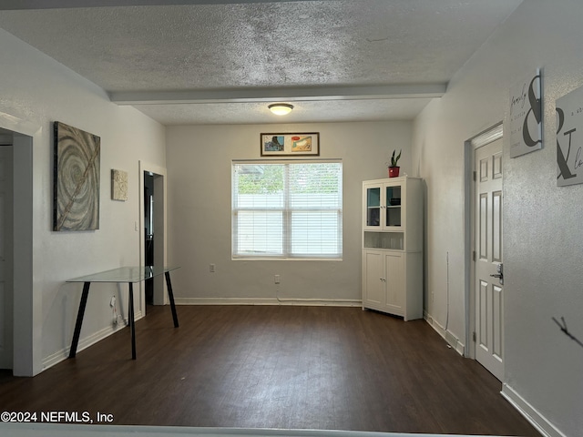 unfurnished room with beamed ceiling, dark wood-type flooring, and a textured ceiling